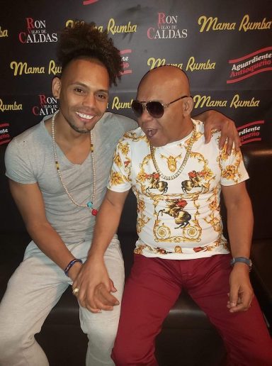 Sandro Reyes y Teodoro Reyes sentados juntos, sonriendo y vistiendo ropa colorida.