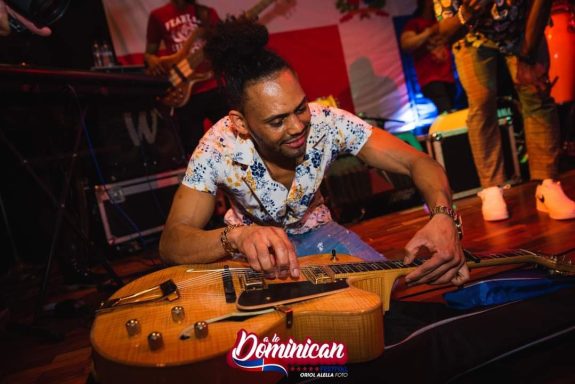 Sandro Reyes tocando una guitarra en un ambiente festivo.